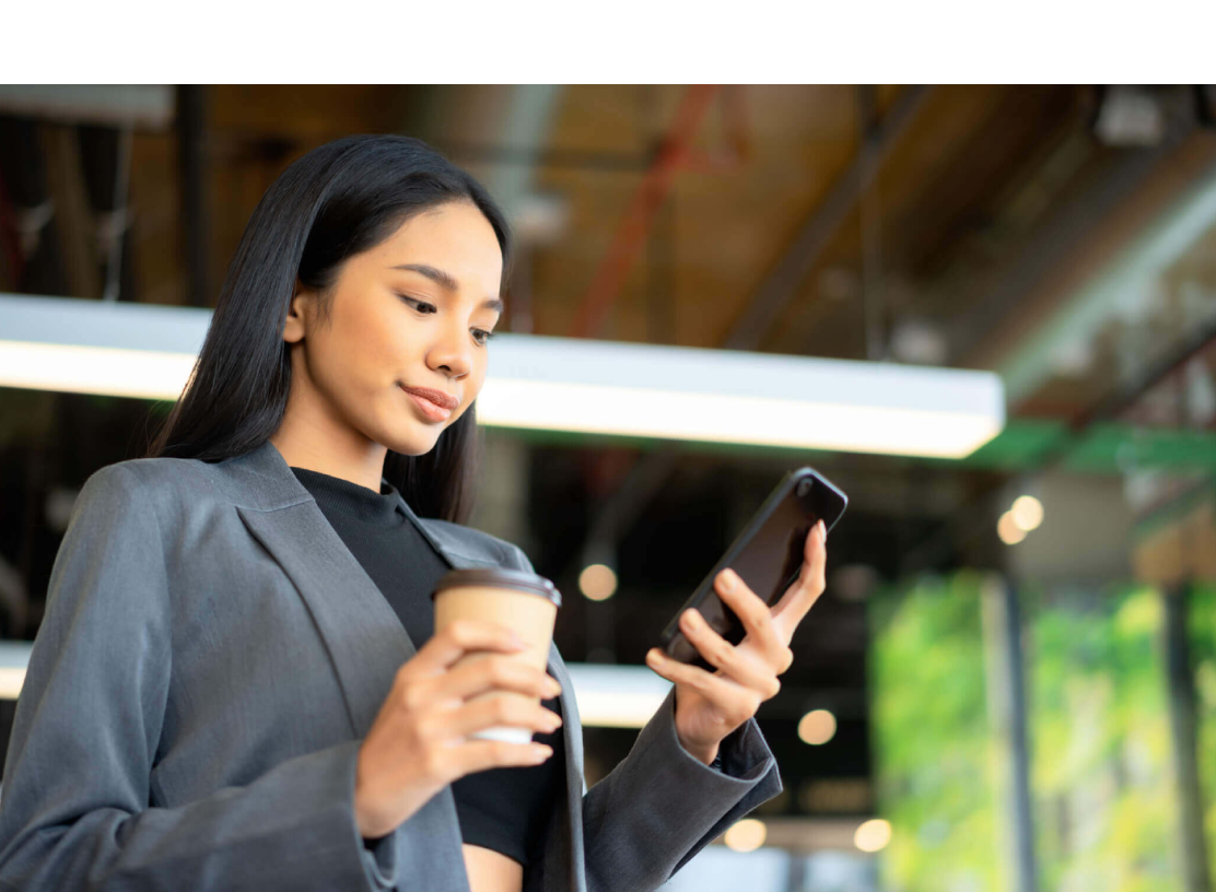 Woman looking at phone and holding a coffee